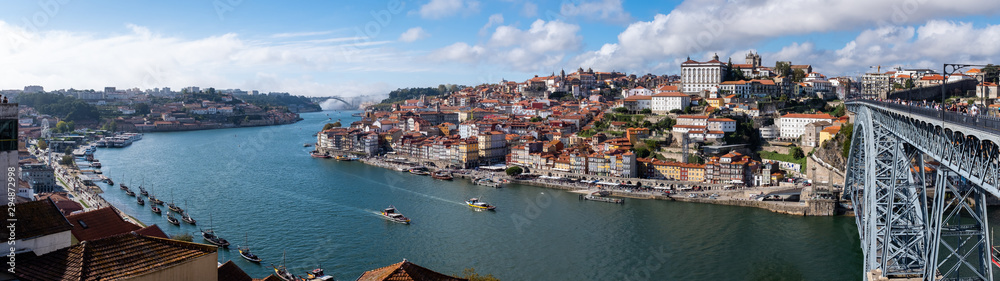 Panoramic view of the Douro River, snaking through the city of Porto with the Ponte Luiz bridge in the foreground and traditional boats tied up on the river.