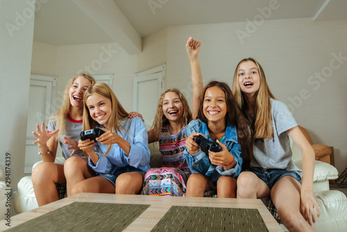 happy group of teenage girls playing video games at home, having fun and relaxing