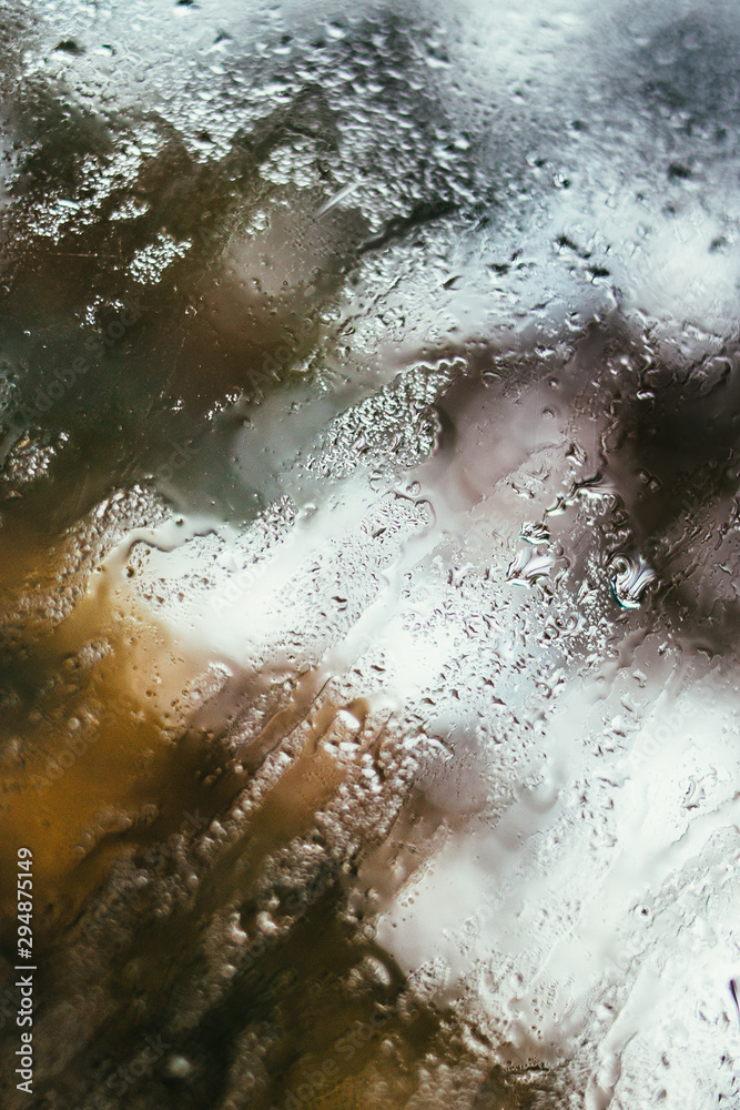 Fototapeta premium Blurred reflection of the street in a misted window, drops of water after rain flow down the glass. Water drops on window. Rainy mood concept.