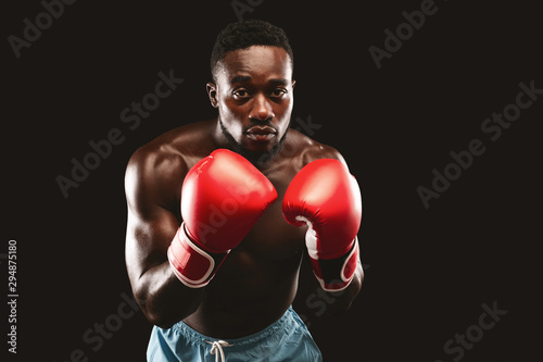 Young muscular boxer in attacking stance over black background