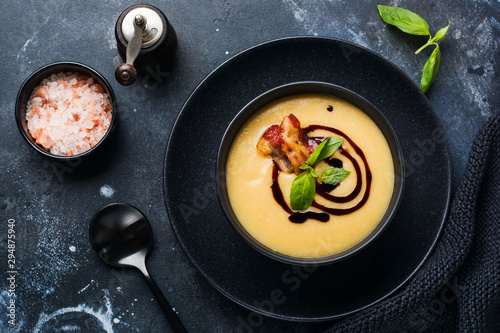 Potato soup cream with bacon and soy sauce in black bowl, on dark old concrete background. Top view.