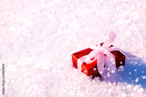 Gift box wrapped on red paper and pink ribbon with lights on snow background. Christmas and New Year holidays celebration concept.