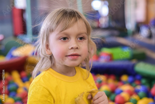 Portrait of a blond boy in a yellow t-shirt. The child smiles and plays in the children's playroom. Ball pool.