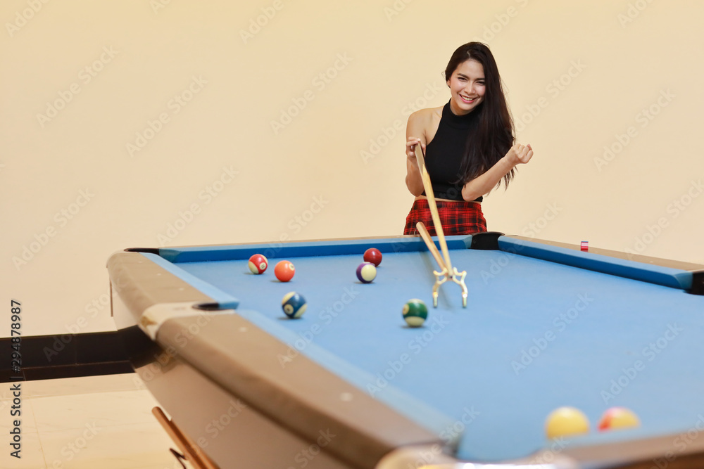 Fototapeta premium beautiful and sexy asian woman in black dress playing billiard or snooker on blue pool table with happy smiling face during holiday vacation