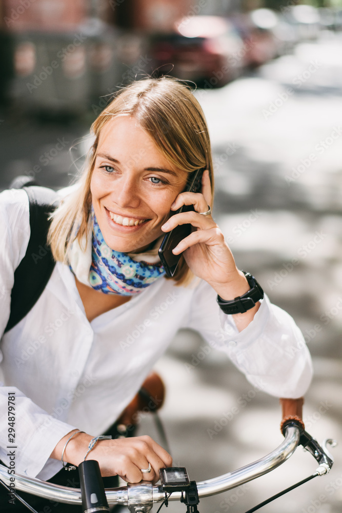 Fototapeta premium Beautiful young woman posing with her bicycle while using phone