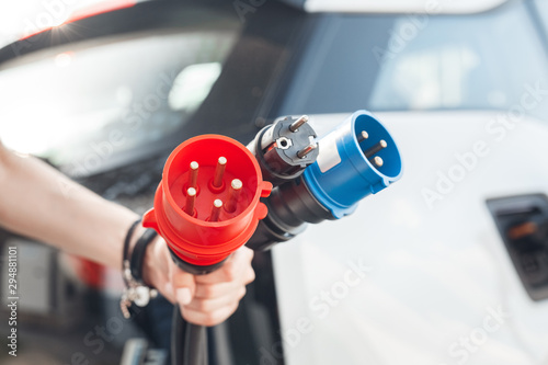 Foto Young adult man holding different power cable supply for charging electric car