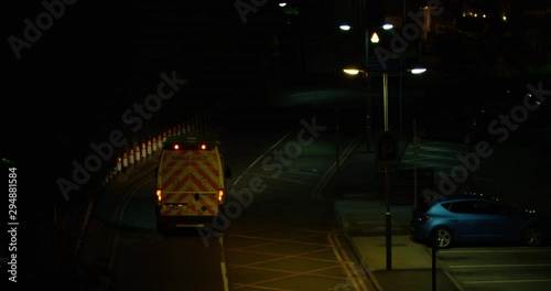  A British Ambulance Driving Down a Dark Road Leaving For An Emergency Late at Night. Driving to an Incident. Dark Dim Empty Road With Very Little Street Lights.