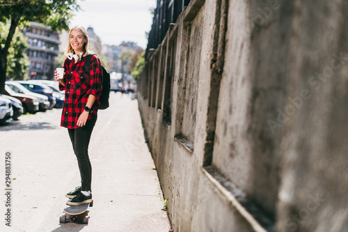 Young woman holding coffee while skating  © JustLife