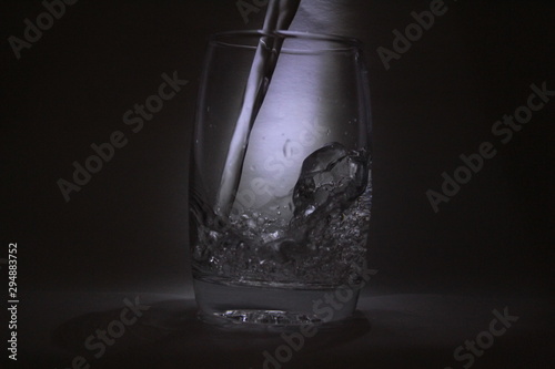 Water falling into the transparent   white glass with black background with some light