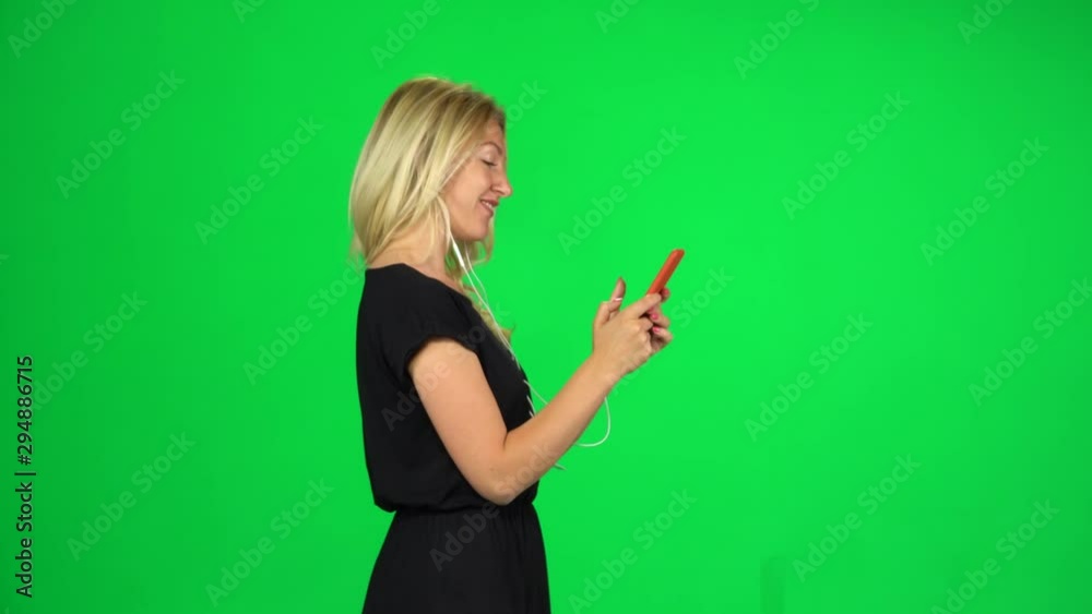 Young woman goes in headphones and texting with smartphone. Chroma Key. Side view Young woman goes in headphones and texting with smartphone. Chroma Key. Side view