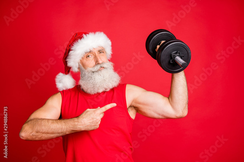 Portrait of cool santa claus sportsman in hat cap with white hairstyle holding dumbbells show fitness effedct routine wearing sportswear isolated over red background