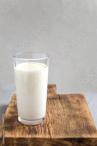Milk in a glass on a wooden stand on a gray background. Side view, copy space. The concept of healthy eating.