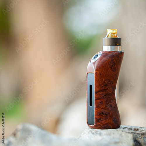 high end rebuildable dripping atomizer with natural stabilized wood regulated box mods on natural timber wood texture background, vaporizer equipment, selective focus photo