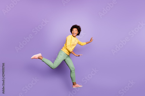 Fototapeta Naklejka Na Ścianę i Meble -  Full size profile side photo of cheerful excited wavy hair girl jump run play catch-up game with friends on spring time wear yellow pullover green pants isolated violet purple color background