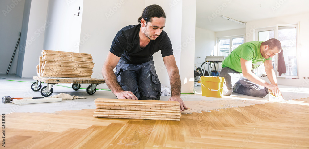 Carpenter on work putting wood parquet pieces. Home construction  - obrazy, fototapety, plakaty 