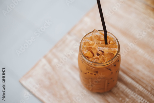 Iced Thai Milk Tea in glass with straw on wooden table in cafe.
