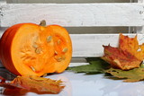 Half an orange pumpkin lies on a white surface. Nearby is a box of white painted wooden boards. Decorated with colorful autumn leaves.