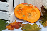 Half an orange pumpkin lies on a white surface. Nearby is a box of white painted wooden boards. Decorated with colorful autumn leaves.