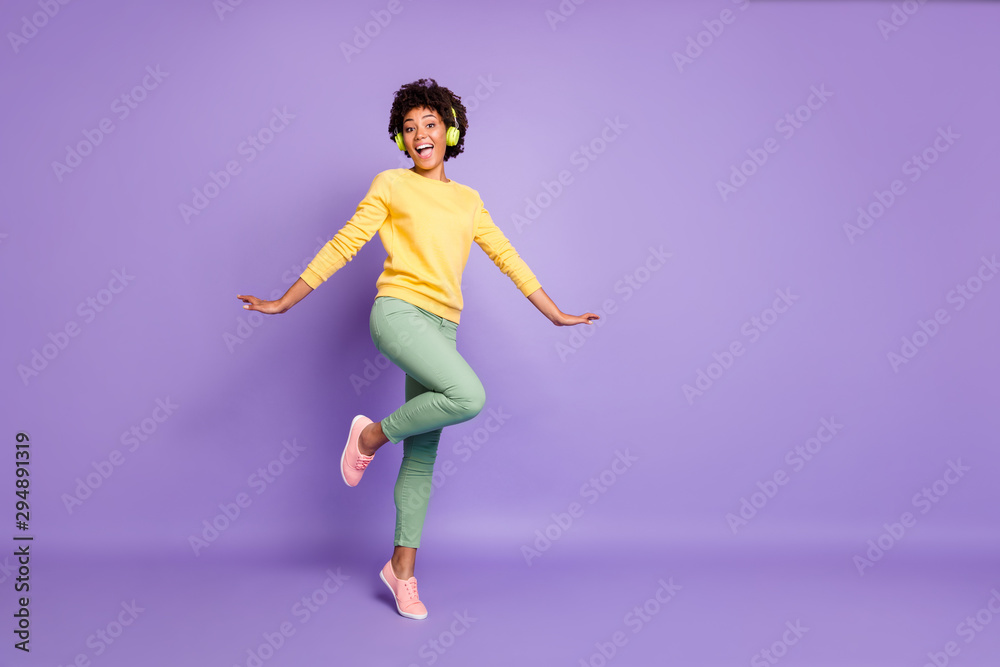 Full length body size turned photo of cheerful positive cute nice charming girlfriend dancing in headphones wearing yellow sweater green pants trousers isolated over violet pastel color background