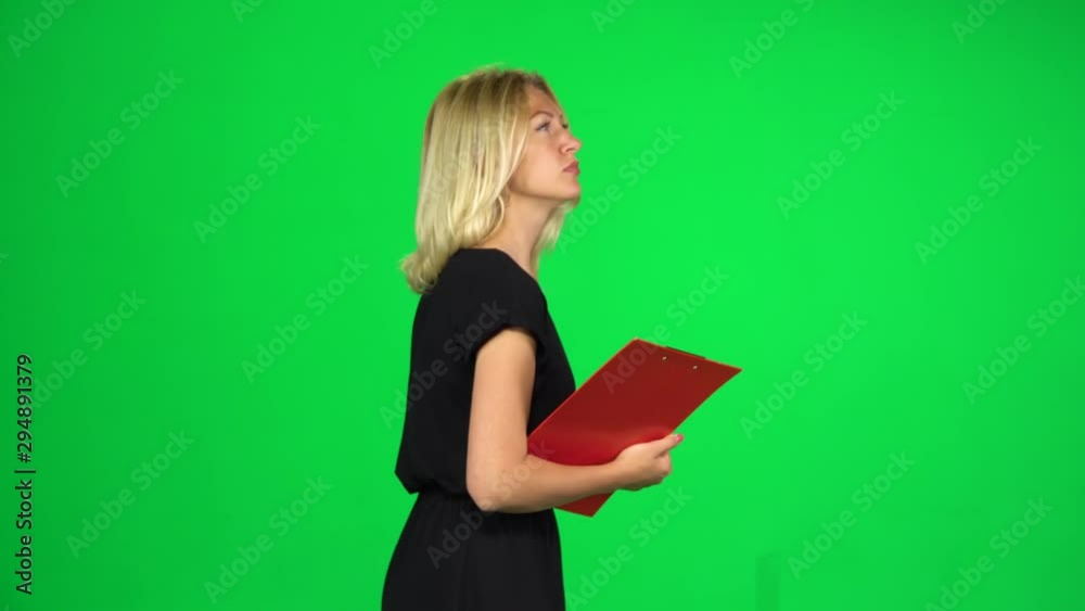 Woman with a red folder goes carefully looking around and taking notes, Chroma Key. Side view Woman with a red folder goes carefully looking around and taking notes, Chroma Key. Side view