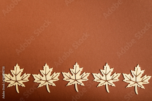 Line with five delicate light brown wooden leaves on textured brown cardboard background, top view with space for text on the right side, flat lay with laser cut wooden objects, selective focus