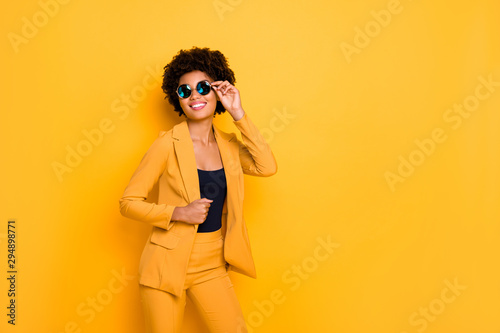 I am gorgeous. Portrait of attractive cheerful afro american lady touch her specs feel content about her beauty wear fashionable clothing isolated over yellow bright color background