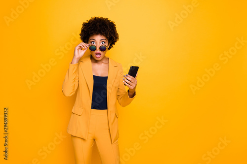 Portrait of shocked afro american girl use smartphone read news on social network account get notification about dislike scream omg wear stylish fashionable clothes isolated yellow color background photo