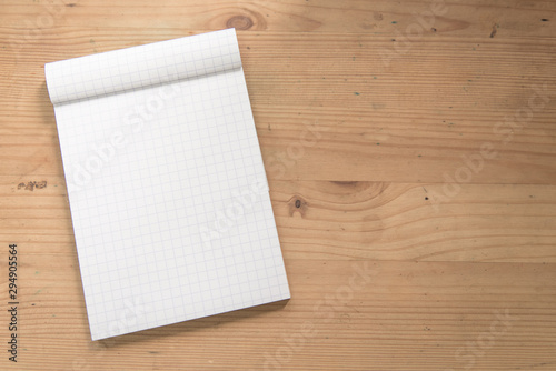 Mock up open blank grid notepad on a wooden table.