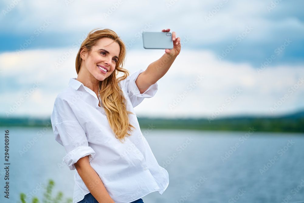 Happy woman taking selfie with smartphone at the lakeside Happy woman taking selfie with smartphone at the lakeside