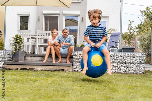 Parents watching son bouncing with hop ball in garden