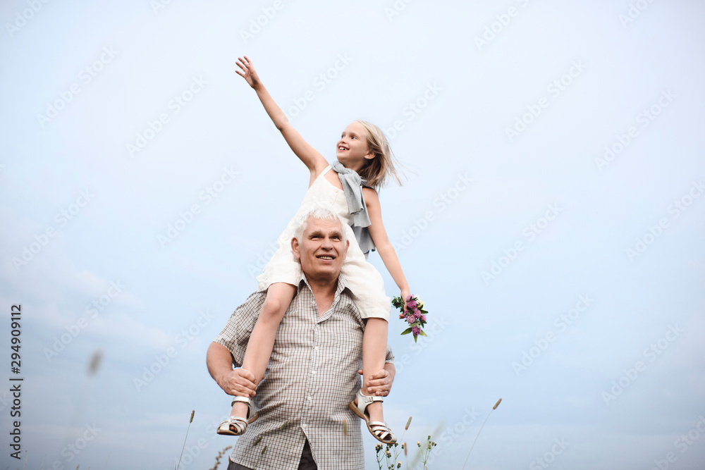 Senior man carrying happy granddaughter on his shoulders in nature Senior man carrying happy granddaughter on his shoulders in nature