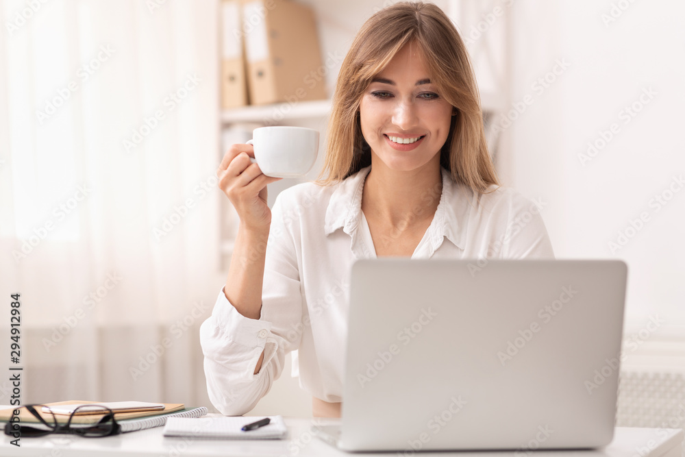 Smiling Businesswoman Holding Coffee Cup Sitting At Laptop In Office Smiling Businesswoman Holding Coffee Cup Sitting At Laptop In Office
