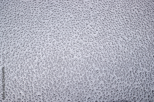 Morning pattern of chaotically arranged drops of water passed the day before rain or dew on the metal front hood of a bluish gray car.