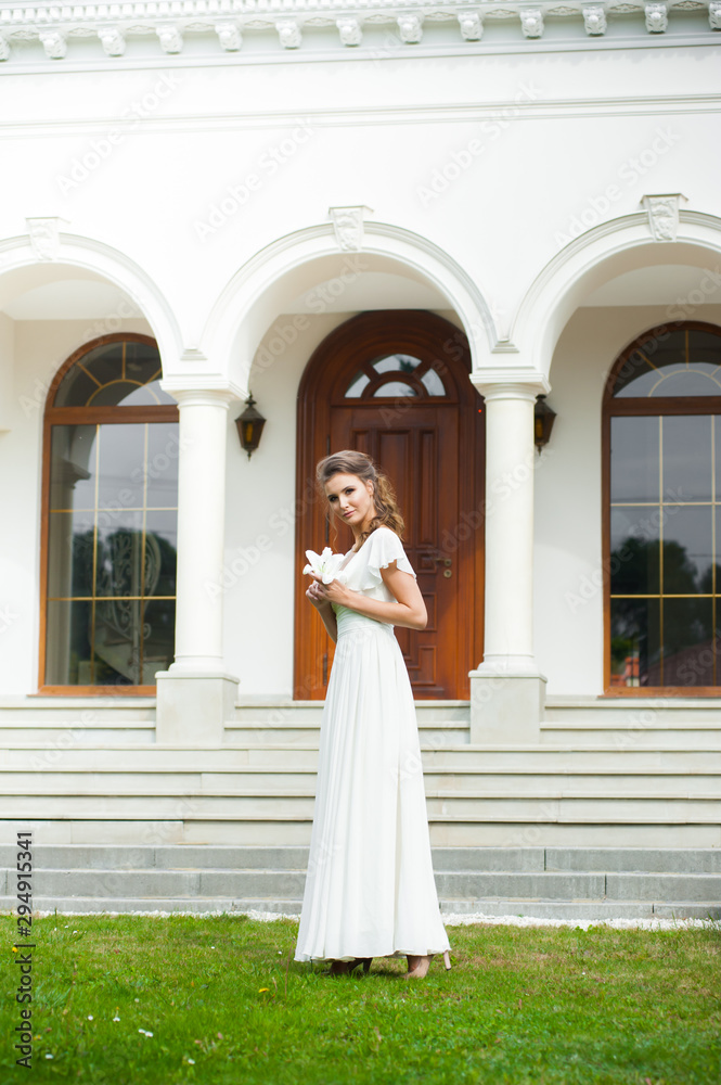 Beautiful young woman walking in long white dress. Tender bride with wedding bouquet.