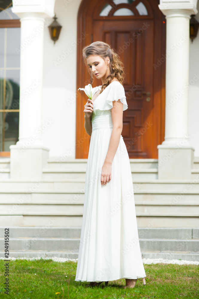 Fototapeta premium Beautiful young woman walking in long white dress. Tender bride with wedding bouquet.