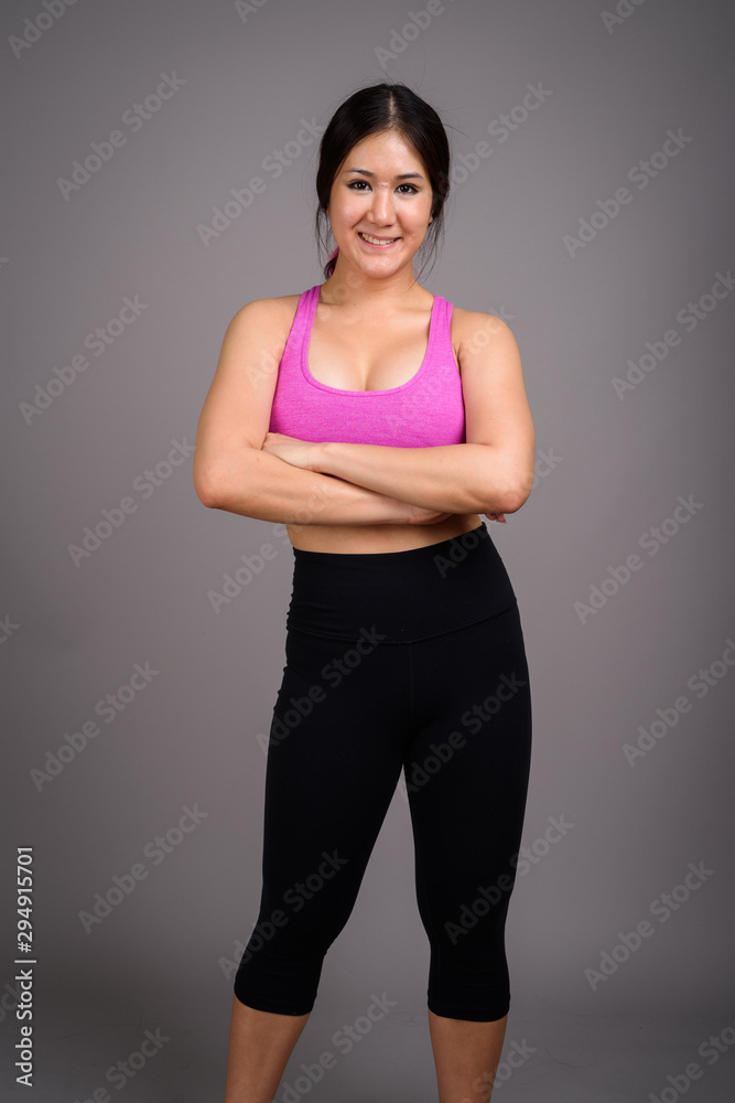 Young beautiful Asian woman ready for gym against gray backgroun
