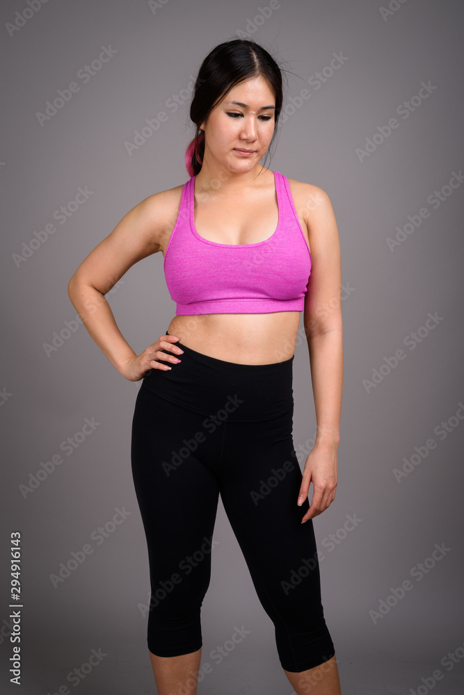 Young beautiful Asian woman ready for gym against gray backgroun Young beautiful Asian woman ready for gym against gray backgroun