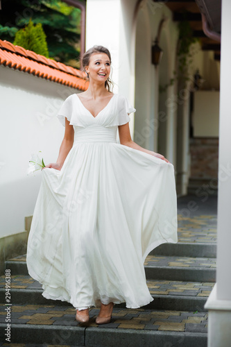 Beautiful young woman walking in long white dress. Tender bride with wedding bouquet.