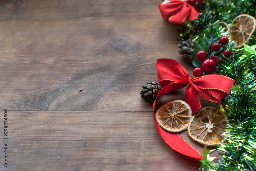Christmas background with decorative composition of green tinsel, dried oranges, red berres, pine cone, gift with red bow and stars on wooden board. Happy new year. Christmas background with decorative composition of green tinsel, dried oranges, red berres, pine cone, gift with red bow and stars on wooden board. Happy new year.