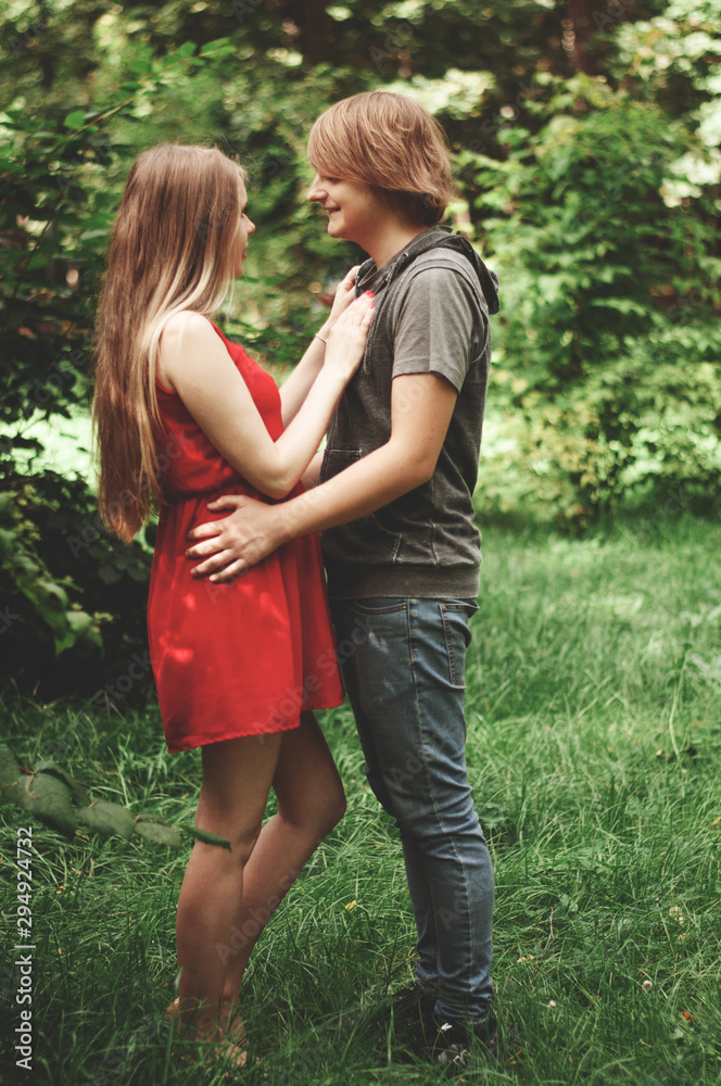 Fototapeta premium Vertical photo. happy married couple Husband hugs a beautiful adult pregnant wife. walks in a park. Second trimester. Holds his hands on her stomach. benefits of walking during pregnancy, 