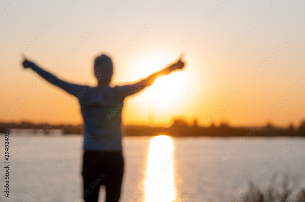 Out of focus. A young man, a hipster, stands on a lake at sunset, enjoys the view while traveling, desolation, enjoyment, harmony.