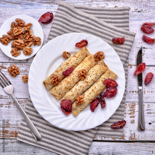 Pancakes, Walnut, Plums. Pancakes with filling on a white plate. Wood background. Rustic style. Rolled up pancakes. Wrapped thin pancakes. Homemade crepes, dried fruits, nuts.