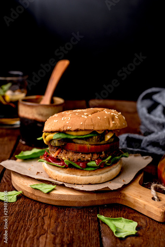Wegański burger z kotletem z ciecierzycy, listkami szpinaku, pomidorem i sosem musztardowym. podany na papierze, na drewnianej desce.
