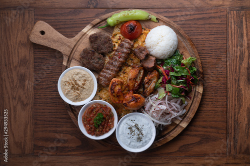 Картината върху платно Mixed turkish kebab plate with rice, vegetables and dip sauces isolated on woode