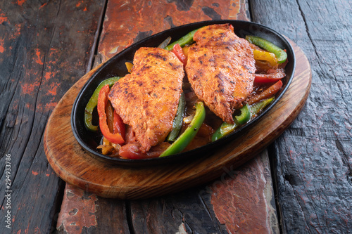 Sizzling chicken fillet with vegetables on rustic wooden table