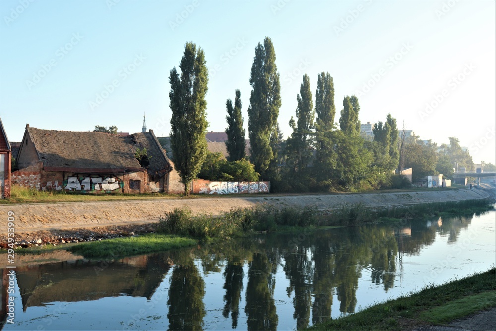 river along which old houses stand and tall trees grow river along which old houses stand and tall trees grow