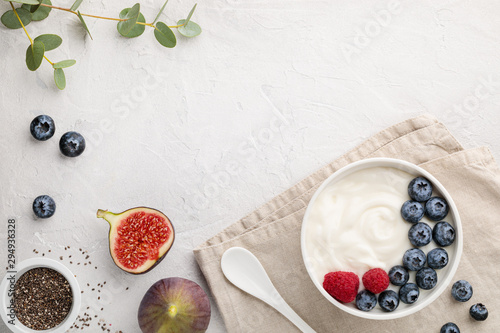 natural healthy superfood fermented yogurt with blueberry, figs, chia seeds and raspberry in white bowl on light gray table. Image is copy space and top view