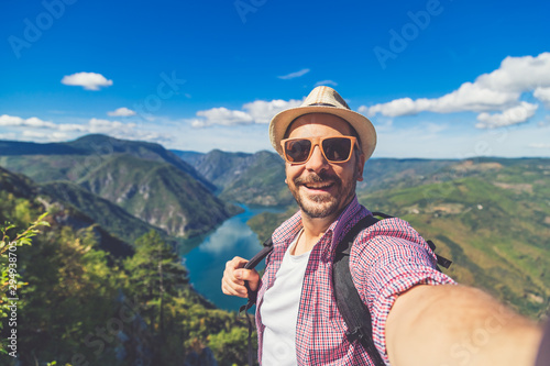 Tableau sur toile Fashionable tourist taking photo of himself while standing on hill above canyon and mountains