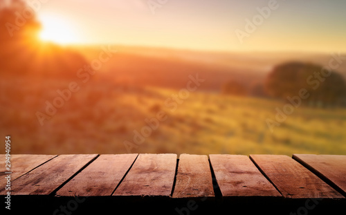 Obraz na płótnie A wooden table top planks product display with a blurred background scene of farmland at sunset. w salonie