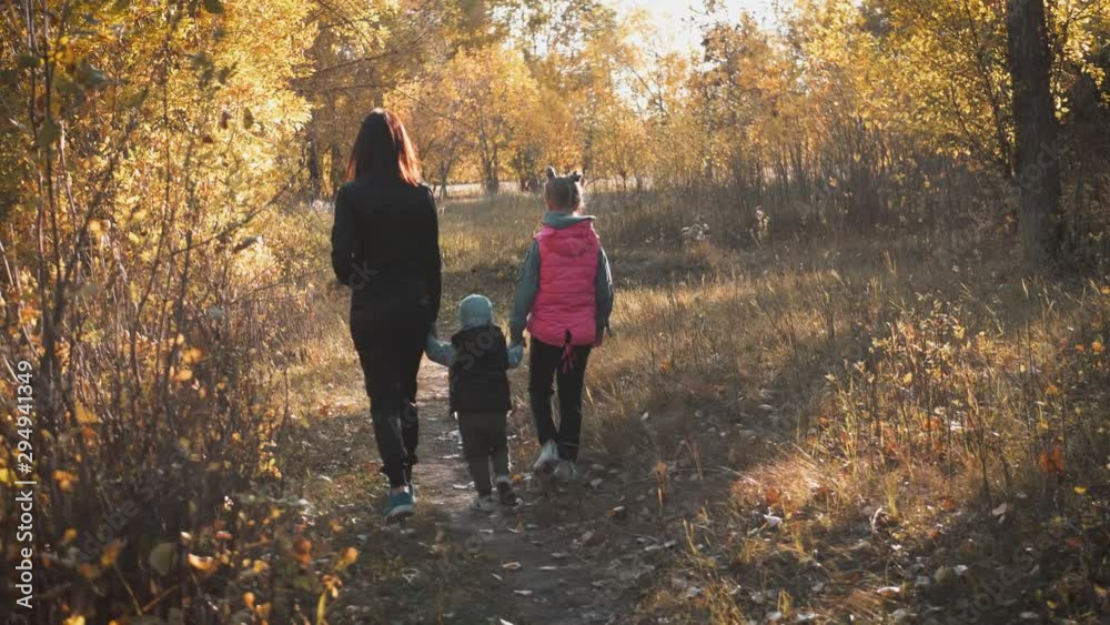 Mother and two children walking in the park and enjoying the beautiful autumn nature. Happy family on autumn walk. Mother and two children walking in the park and enjoying the beautiful autumn nature. Happy family on autumn walk.